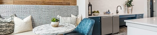 A blue chair sits in a modern kitchen with a white table and a painting on the wall.