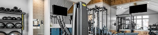 A gym with a variety of equipment including a squat rack, weight bench, and a flat screen TV.