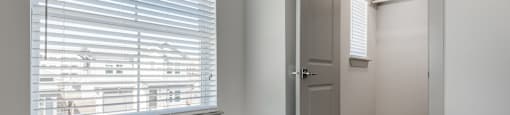 A room with a carpeted floor, a window with blinds, and a door.