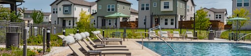 A pool area with sun loungers and a row of houses in the background.