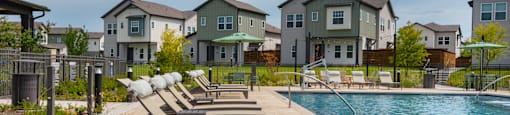 A pool with lounge chairs and apartment buildings in the background.