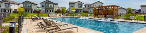 A swimming pool surrounded by lounge chairs and a row of houses in the background.