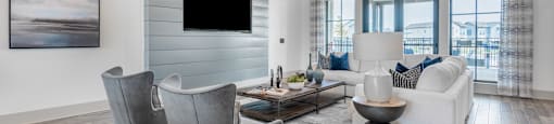 A modern living room with a grey sofa, a grey armchair, a coffee table, and a flat screen TV mounted on the wall.