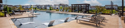 A large outdoor swimming pool with a bench area and a waterfall feature.