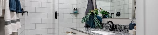 A bathroom with a white tiled shower and a marble countertop.