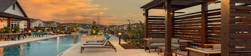 A poolside area with a wooden pergola and lounge chairs.