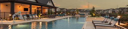 A swimming pool with lounge chairs and a house in the background during sunset.