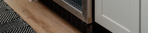 A modern stainless steel oven with wooden slats is built into a white kitchen cabinet.