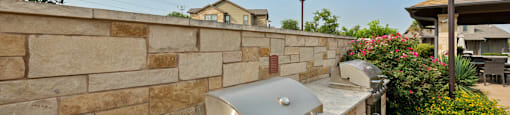 an outdoor kitchen with a stone wall and a grill