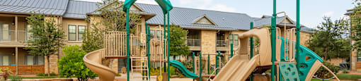 a playground with two slides and a climbing structure in front of an apartment building