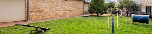 a park with a seesaw and a bench in front of a brick building