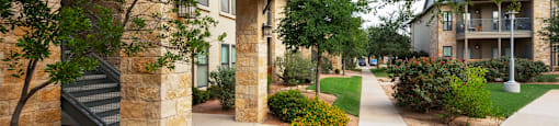 a walkway with trees and bushes in front of a building