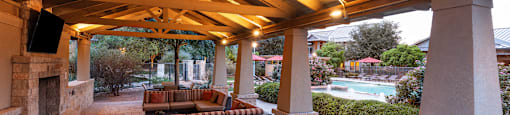 a covered patio with a fireplace and a wooden ceiling with exposed beams