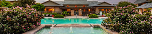 a large swimming pool surrounded by bushes and trees with a building in the background
