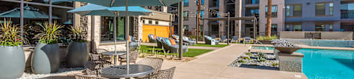 A patio with a table and chairs is surrounded by a pool and buildings.