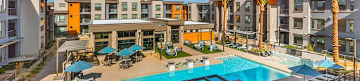 A large swimming pool is surrounded by sun loungers and umbrellas in a sunny courtyard.