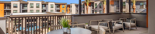 A patio with a table and chairs overlooking a pool and buildings.