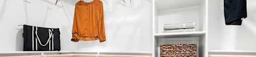 A white closet with a brown shelf and clothes hanging.