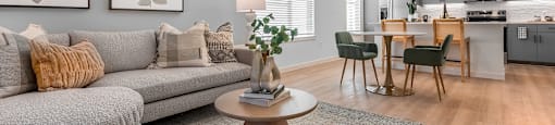A modern living room with a grey sofa, a coffee table, and a dining area in the background.