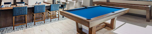 A pool table is in the middle of a room with a bar and chairs.