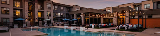 A swimming pool in front of a building with lights on.