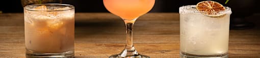 Three different cocktails are displayed on a wooden table.