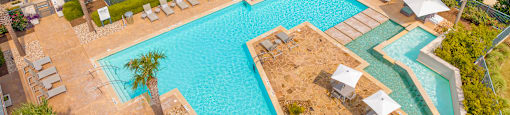 an aerial view of a resort style pool with lounge chairs and umbrellas