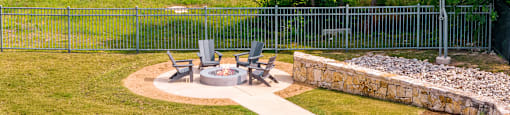 a fire pit in the middle of a grassy area with chairs and a stone wall