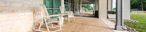 a pair of rocking chairs sit on a porch in front of a building