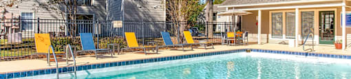 a swimming pool with yellow chairs and a house in the background