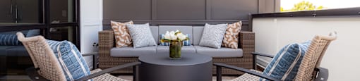 A table with two chairs and a sofa with cushions on a wooden deck.