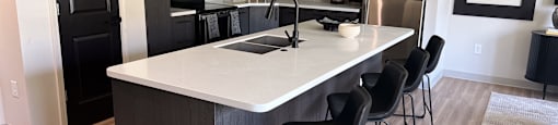 A kitchen with a white island and black chairs.