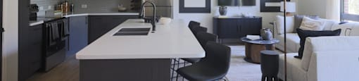 A modern kitchen with a white island and black chairs.