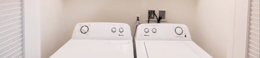 a white laundry room with two washers and a dryer