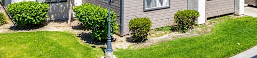 a gray and white building with a lamp post in the middle of a grassy areaat Lincoln Park Apartments, Corona, 92882