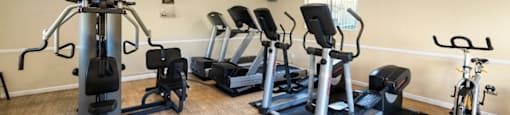 A gym with a variety of equipment including treadmills, stationary bikes, and weight machines. at The Oaks Apartments, Upland