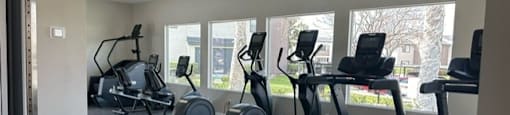 a gym with cardio equipment and windows in a buildingat Lincoln Park Apartments, Corona California