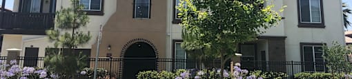the front of an apartment building with trees and flowers