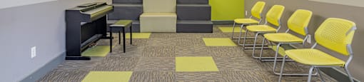 a waiting room with yellow chairs and a piano at International Village UCR Student Housing, Riverside California