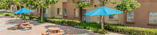 a courtyard with tables and umbrellas in front of an apartment building at International Village UCR Student Housing, Riverside, CA
