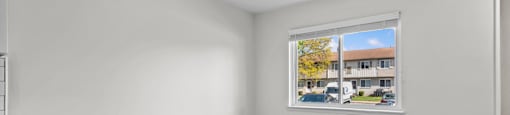 A room with a window showing a view of a building and trees outside.