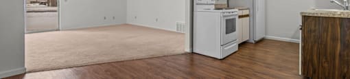 an empty living room with a kitchen with a stove and refrigerator