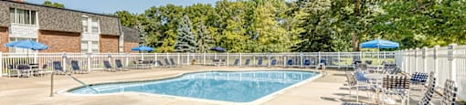 A sunny day at the pool with chairs and trees in the background.