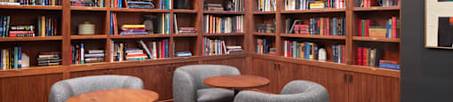 A room with a bookshelf filled with books and a few grey chairs.