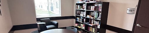 A room with a round table and chairs and a bookshelf.