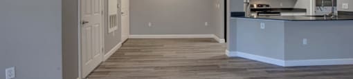 an empty room with a kitchen in the background