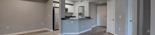 an empty living room with a kitchen in the background