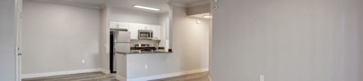 a living room with a ceiling fan and a kitchen in the background