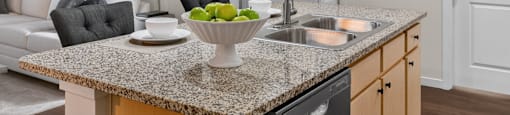 A kitchen with a granite countertop and a bowl of green apples on it.