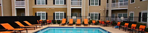 a swimming pool in front of an apartment building with orange chairs